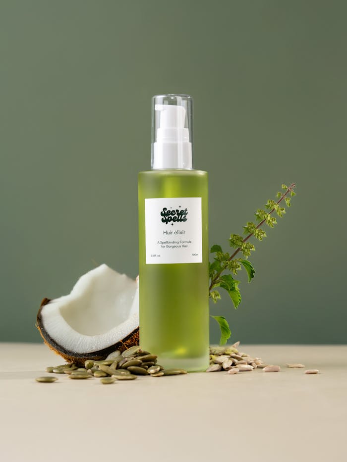 Green hair elixir bottle with coconut and herbs on a minimalist backdrop.